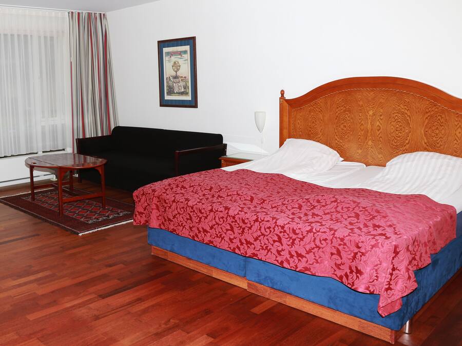 A bedroom with a wooden bed, a black sofa, a small table, and a window with curtains.