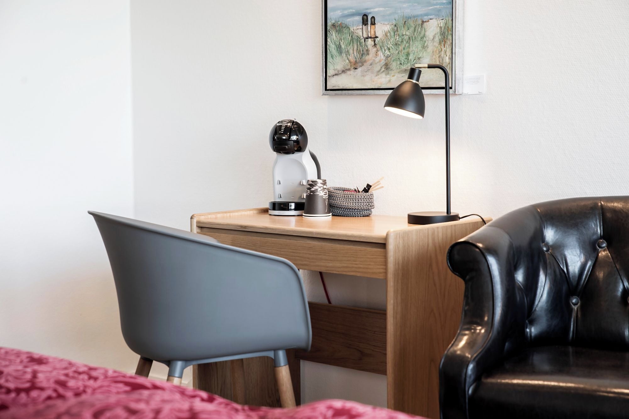 A neatly arranged workspace with a desk, a laptop, a lamp, and a cozy chair.