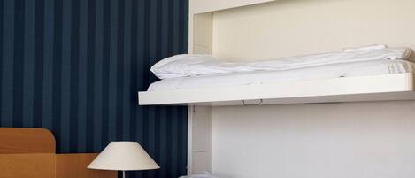 Una habitación de hotel con una cama litera, una mesita de noche con lámpara y papel tapiz a rayas.