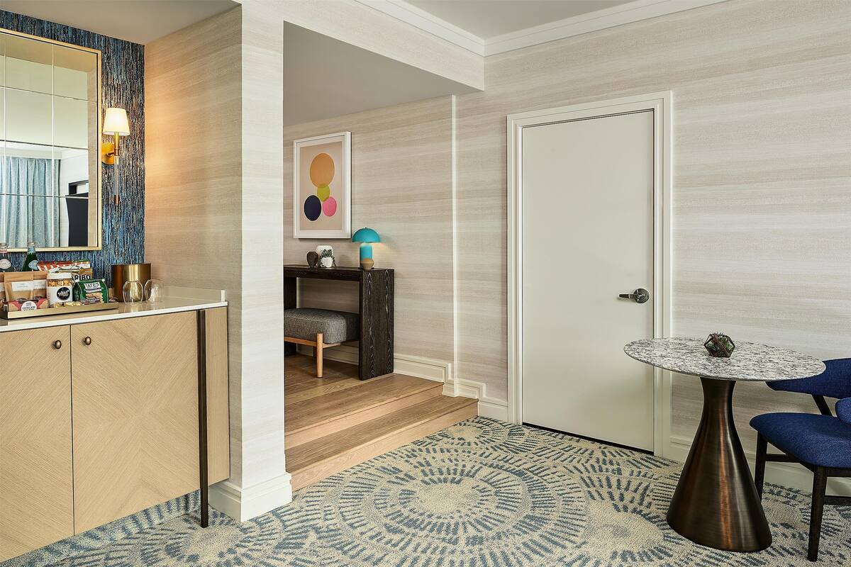 A modern hotel room with a wooden cabinet, a round table, a blue chair, and a patterned rug.