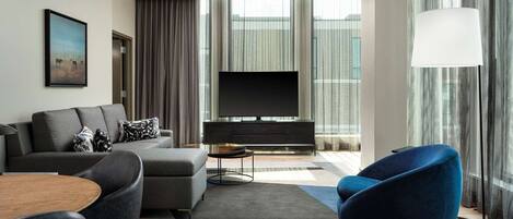A modern living room with a grey sofa, a blue armchair, a coffee table, and a flat-screen TV.