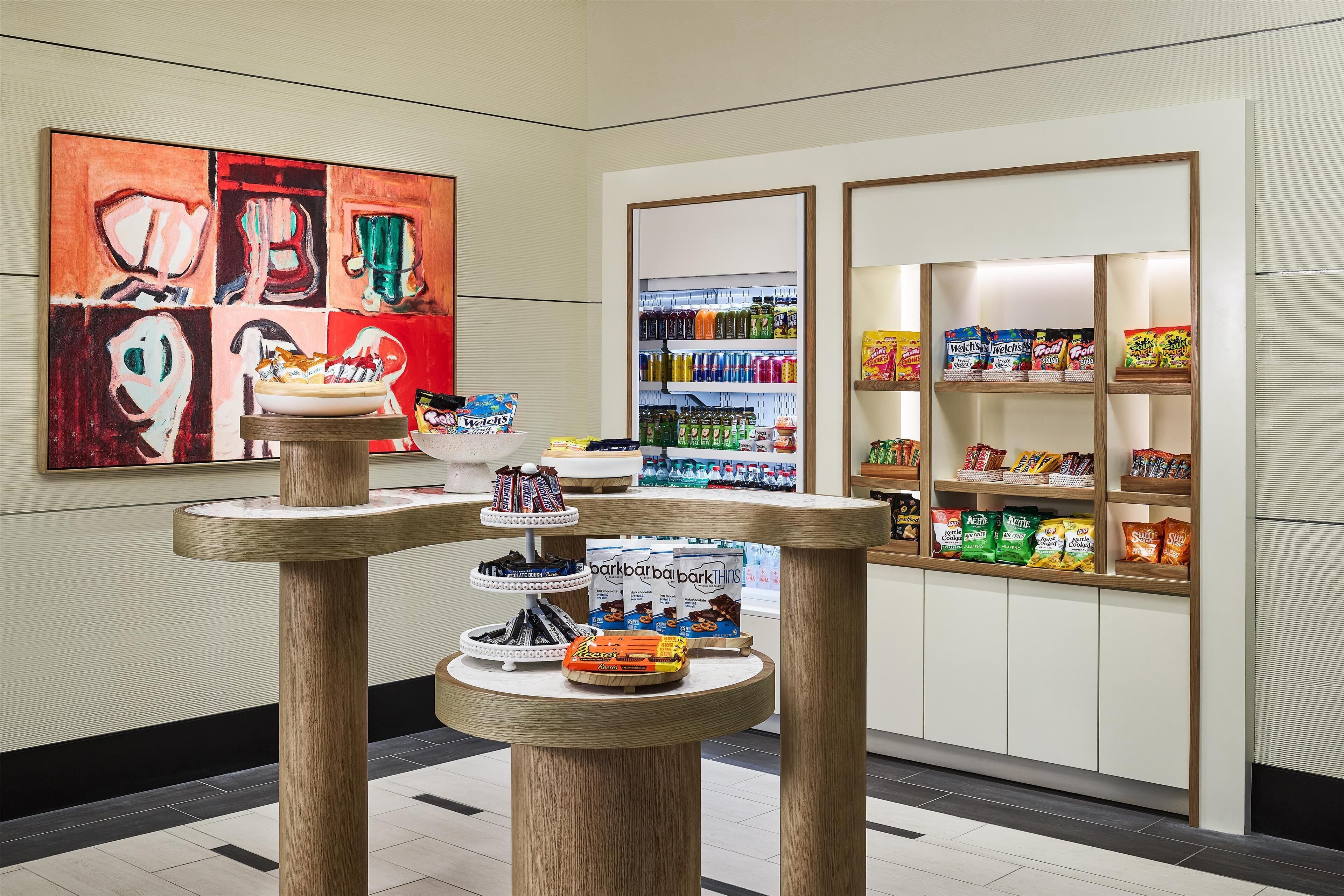 Ein modernes Interieur mit einem zentralen Tisch, der verschiedene Snacks präsentiert, und einem farbenfrohen, abstrakten Gemälde an der Wand.