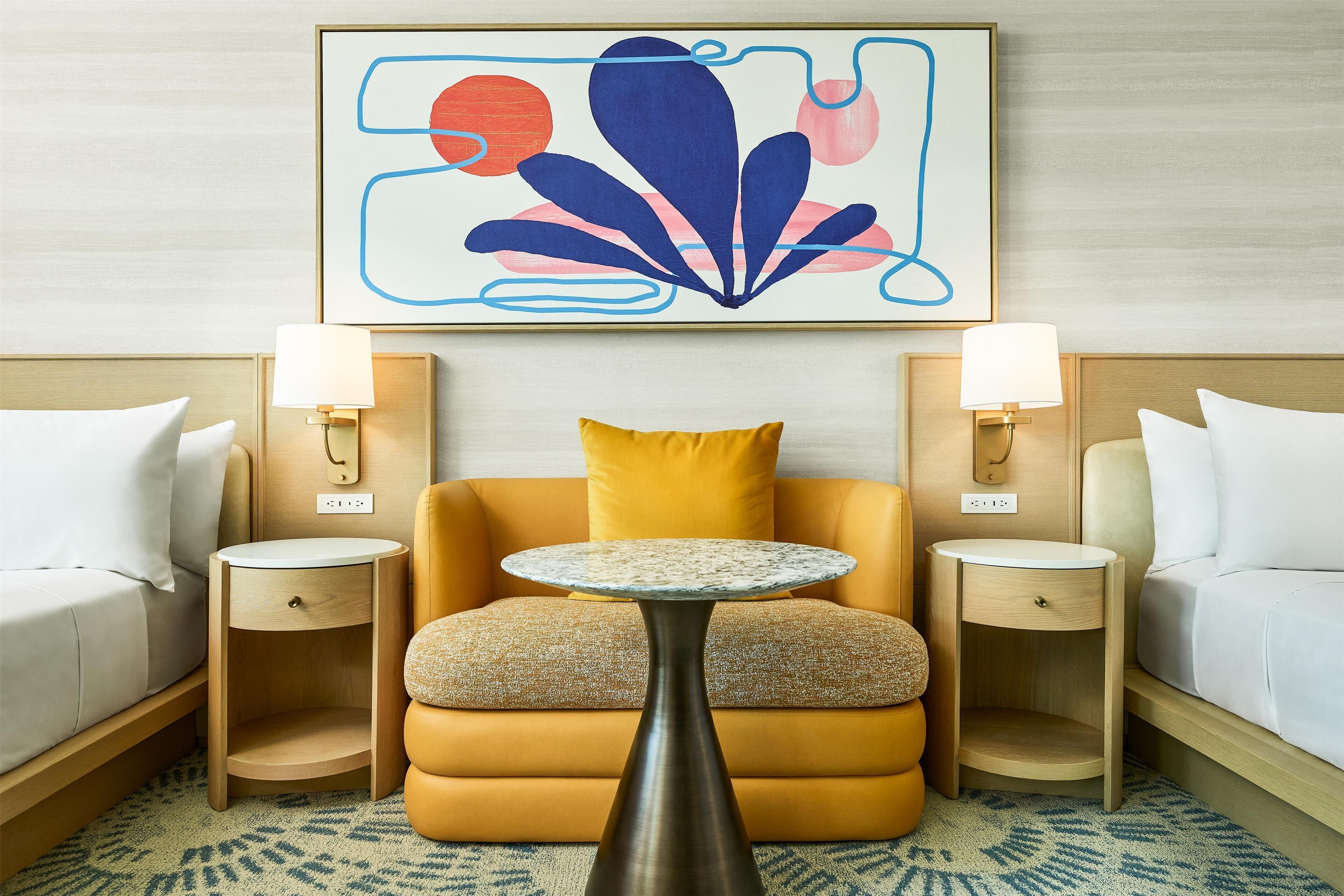 A hotel room with a sofa, two bedside tables with lamps, a small round table, and a large abstract painting on the wall.
