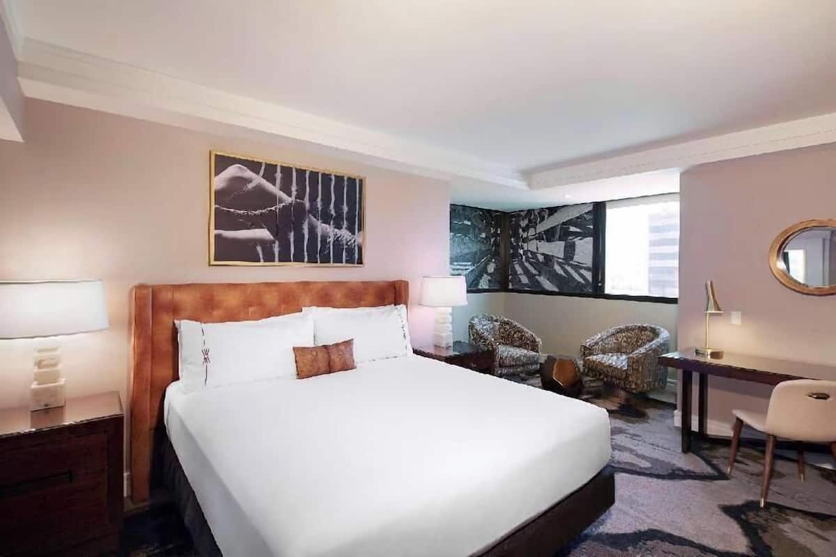 A hotel room with a large bed, a desk, two chairs, a mirror, and artwork on the walls.