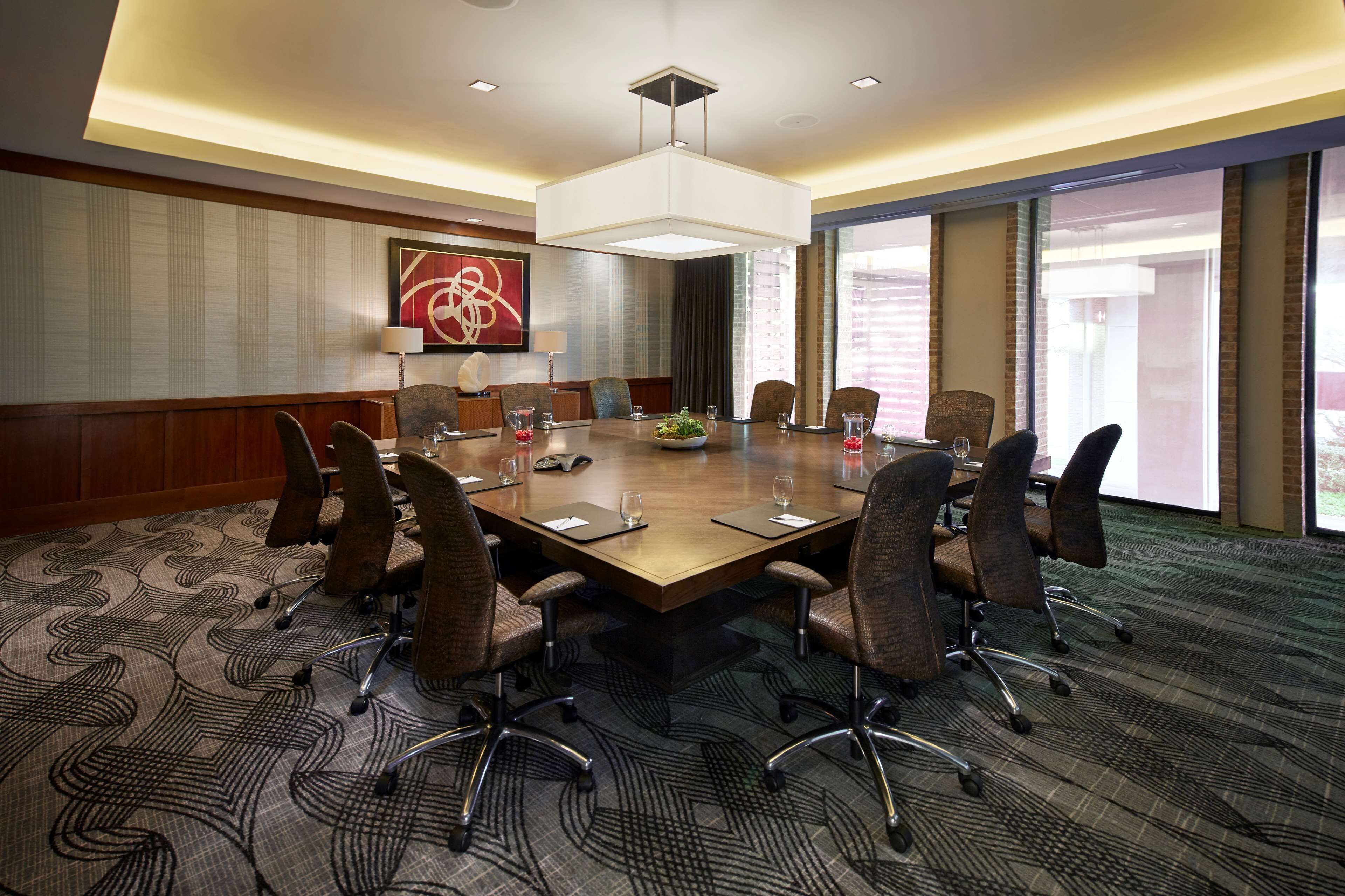 A conference room with a large table, eight chairs, a modern chandelier, and a large window with a view.