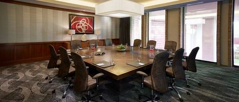 A conference room with a large table, eight chairs, a modern chandelier, and a large window with a view.