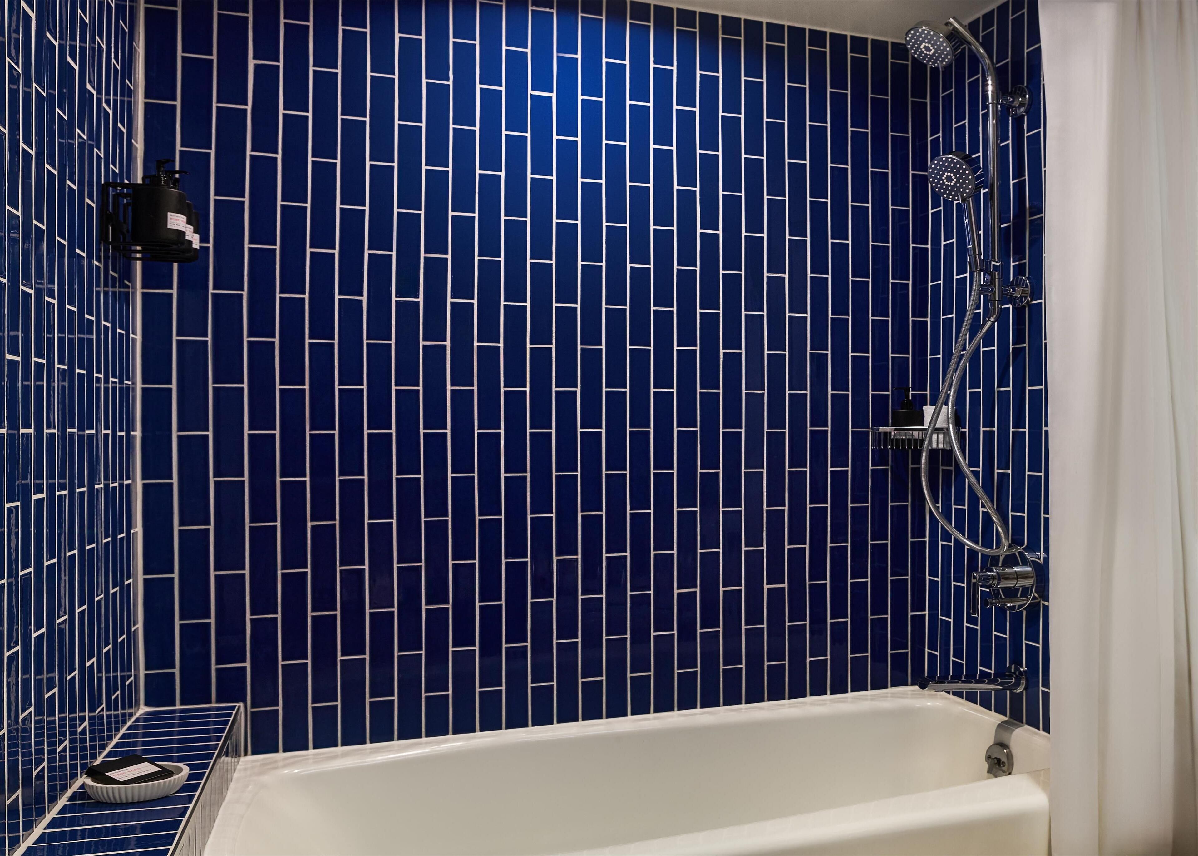 A bathroom with a white bathtub, a shower with a handheld showerhead, and a blue-tiled wall.