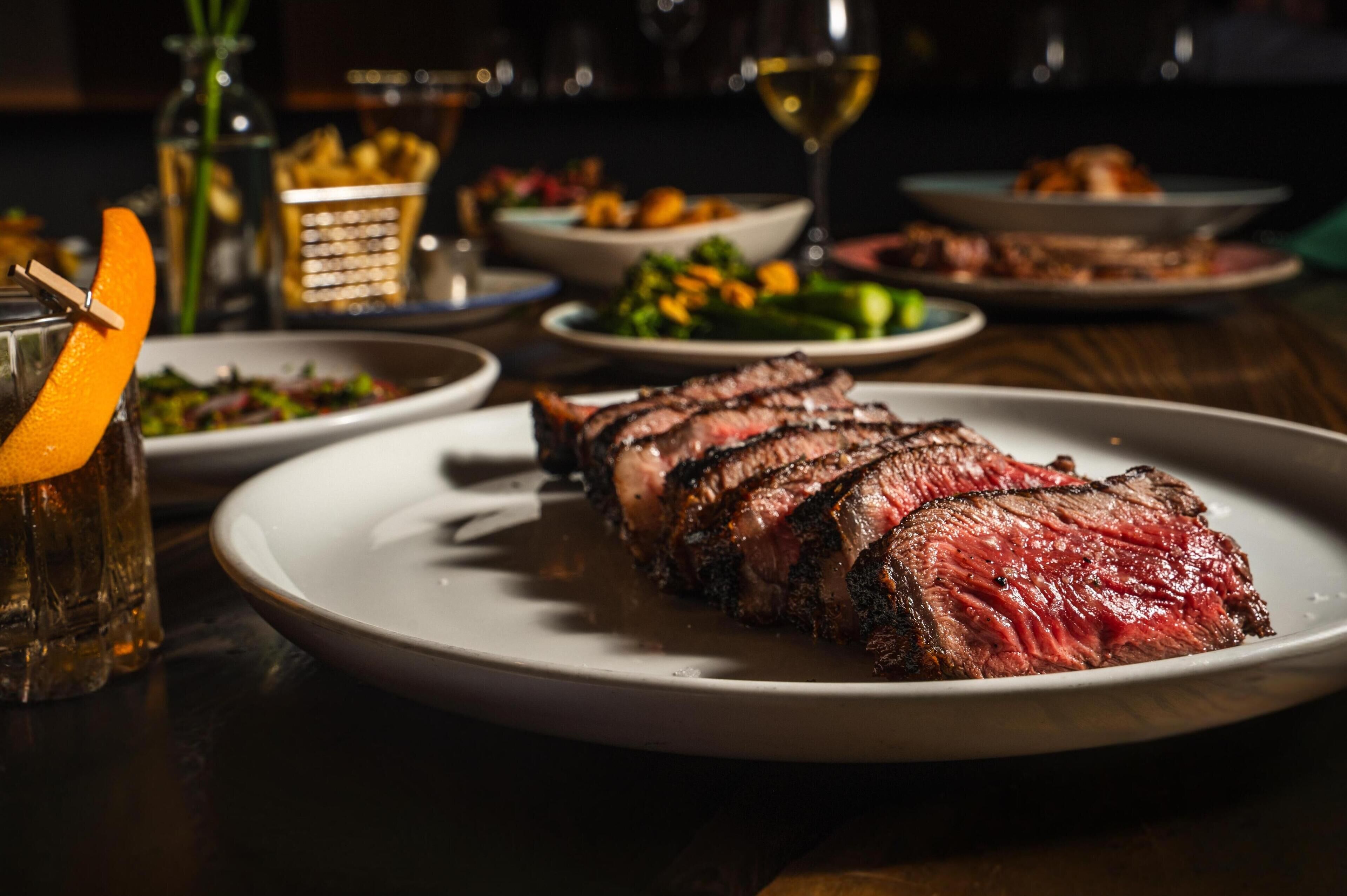 Un plato de carne con una copa de vino y una ensalada al fondo.