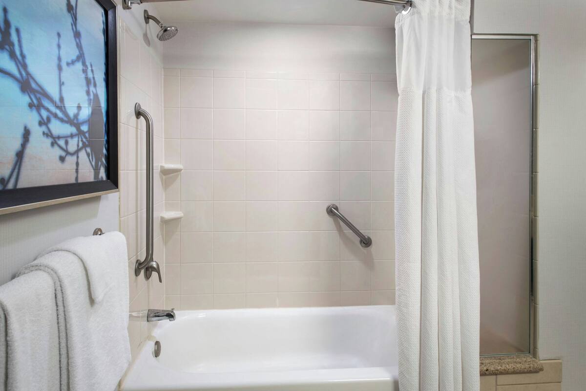 Un baño con bañera, barras de apoyo y cortina de ducha.