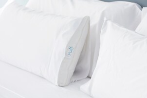 Una cama con ropa de cama y almohadas blancas, una de ellas con un nombre de marca visible.