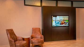 Två bruna läderfåtöljer och en digital skärm i en entréhall.