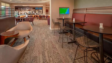 Un vestíbulo de hotel con zonas de estar, un bar y un televisor que muestra un mapa.