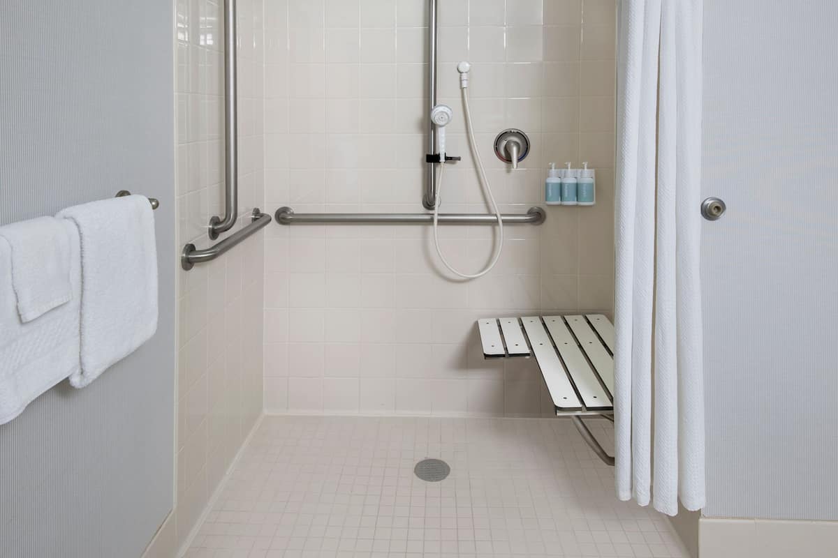 Zona de ducha con barra de apoyo, asiento y toallero.