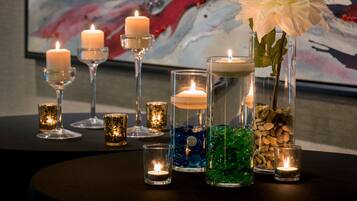 A table with various candles in glass holders, including a white flower in a tall glass container.