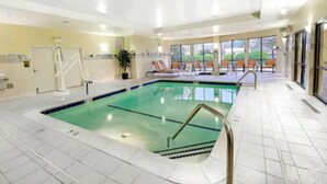 Una piscina interior con carriles delimitados, una silla de socorrista y una tumbona al borde de la piscina.