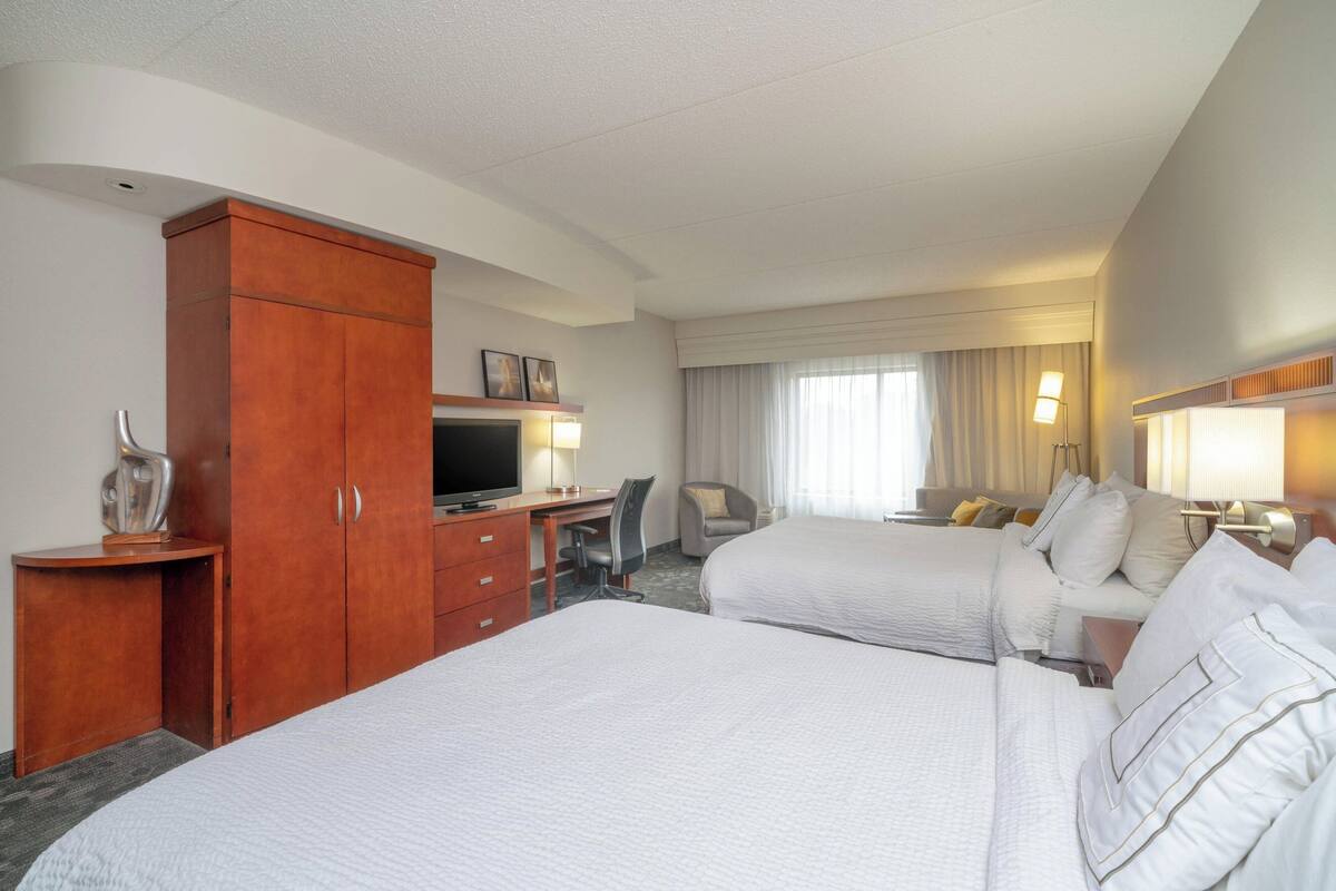 A hotel room with two beds, a desk, a television, and a wardrobe.