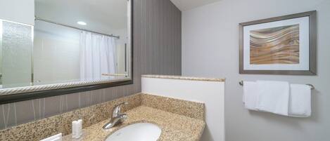 Un baño con lavamanos de encimera de granito, un espejo grande y una obra de arte enmarcada en la pared.