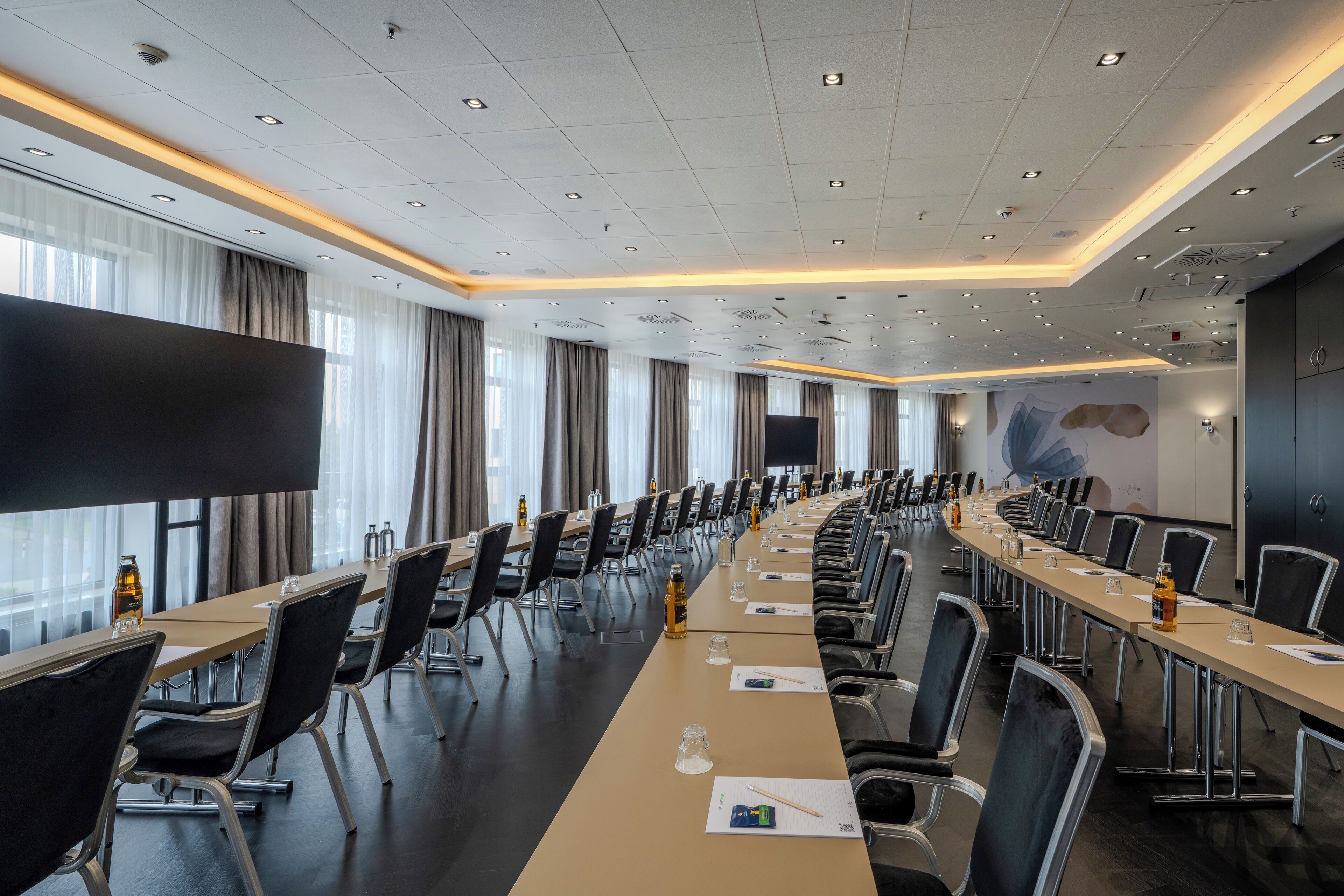 Un salón de conferencias con una larga mesa, sillas y una pantalla grande.