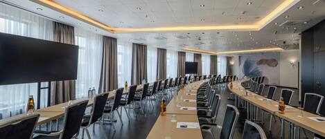A conference room with a long table, chairs, and a large screen.