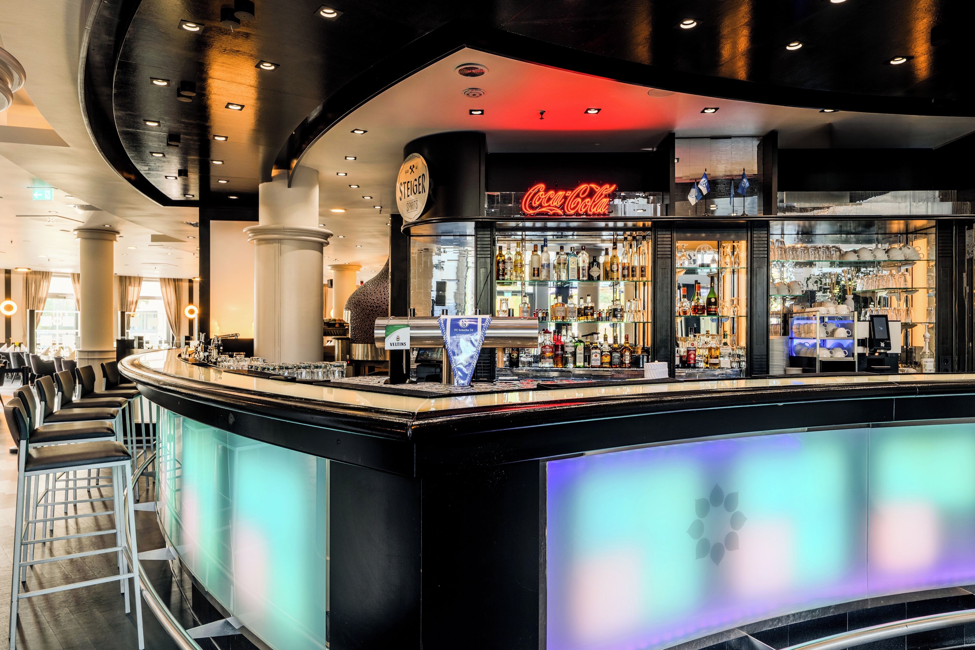 A bar area with a Coca-Cola sign, a variety of liquor bottles, and a modern bar counter.