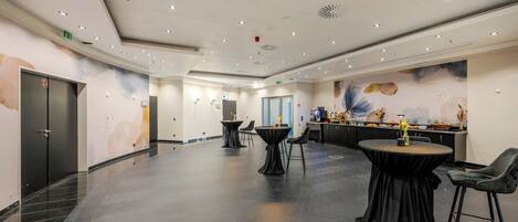 A spacious hotel lobby with a modern design, featuring a reception area, several tables, and chairs.