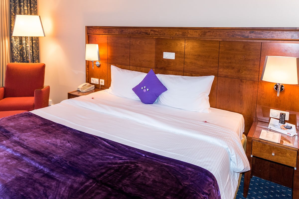 A hotel room with a bed, a nightstand, a telephone, and a chair.