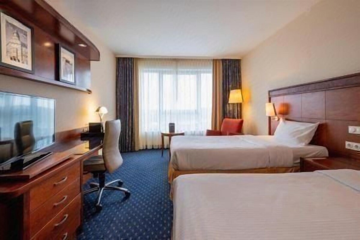 A hotel room with two beds, a desk, a chair, a television, and a window with curtains.