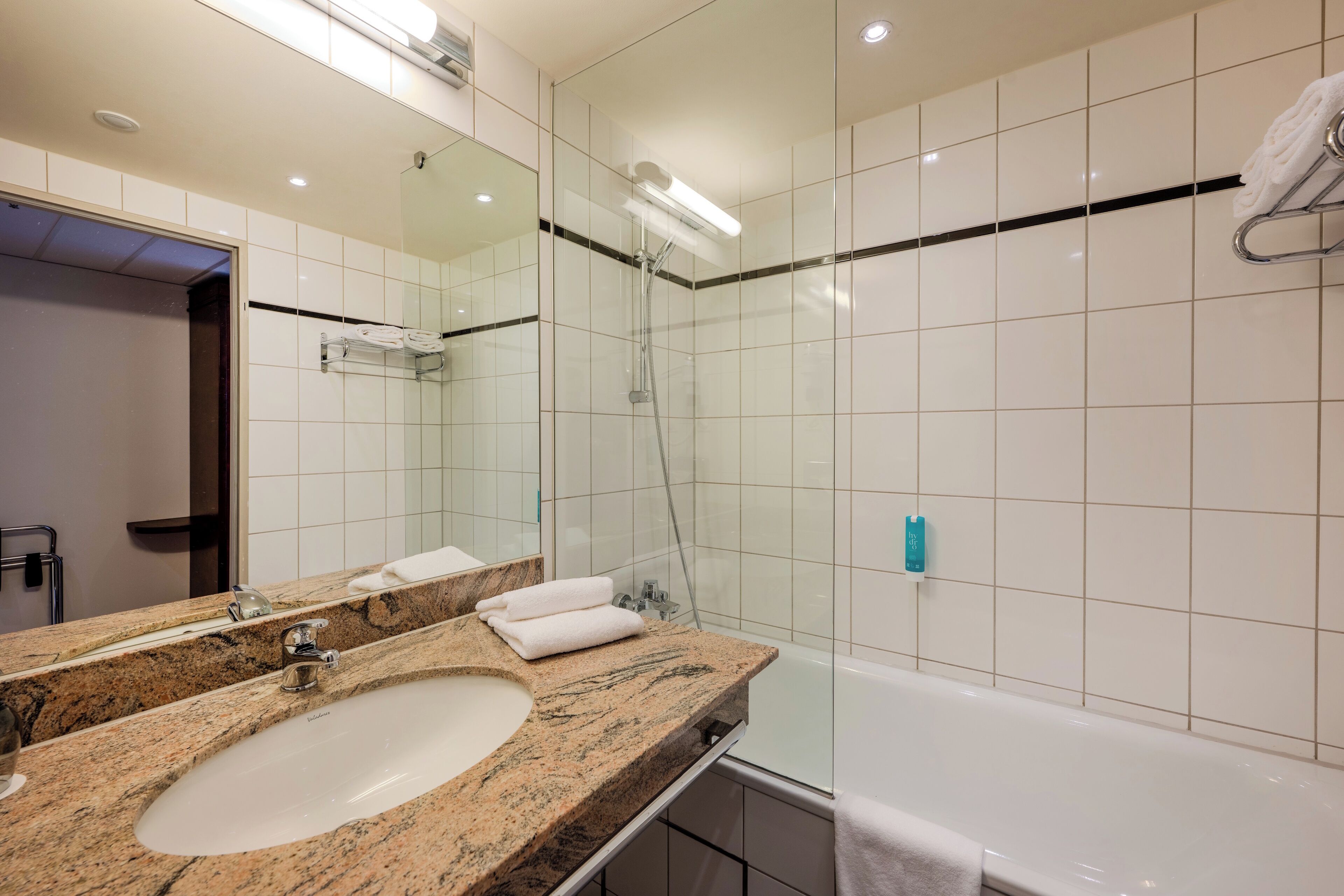 A modern bathroom with a granite sink, a large mirror, a glass-enclosed shower, and a white bathtub.
