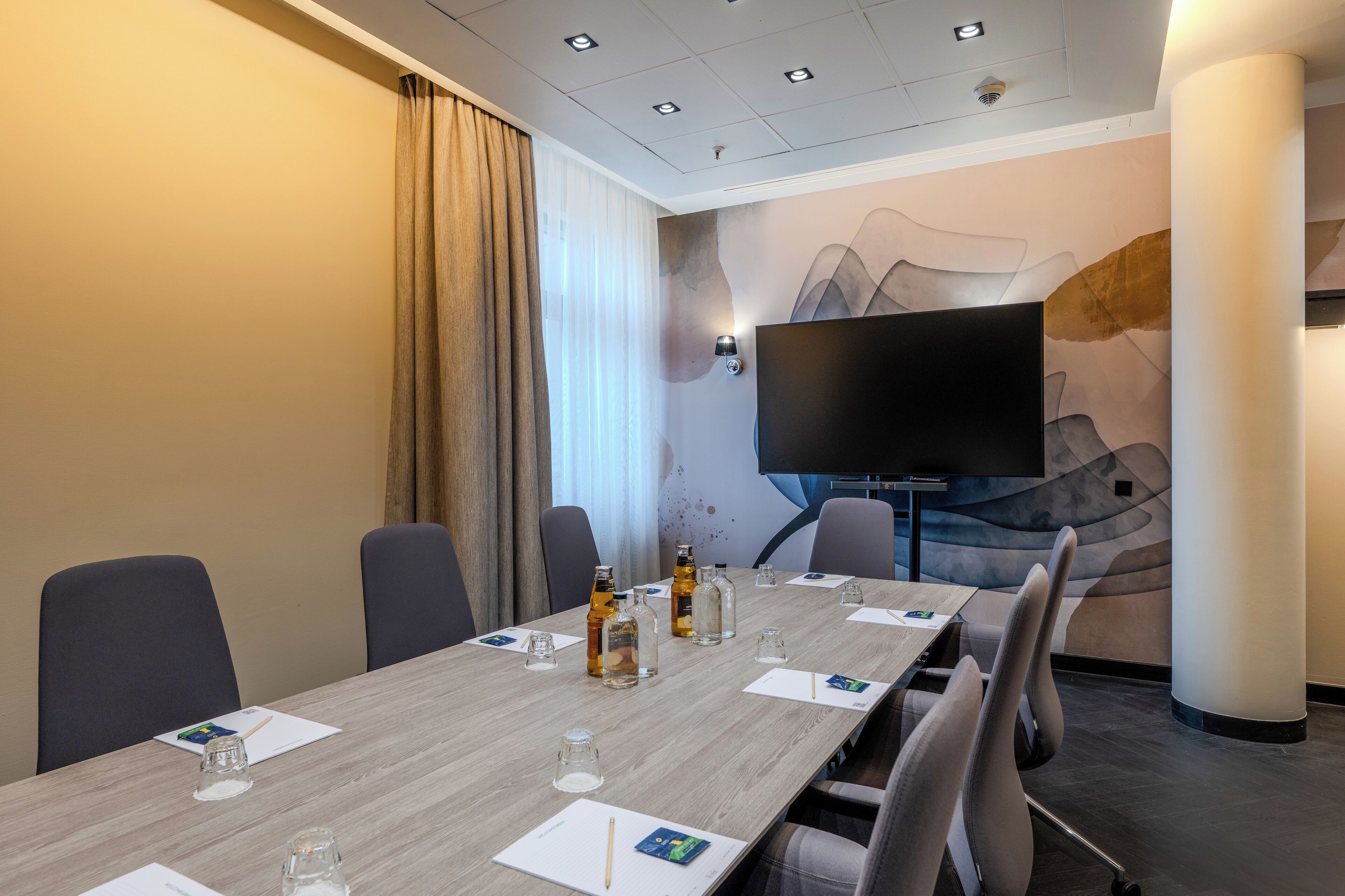A conference room with a long table, chairs, a flat-screen TV, and a decorative wall.