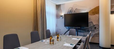 A conference room with a long table, chairs, a flat-screen TV, and a decorative wall.