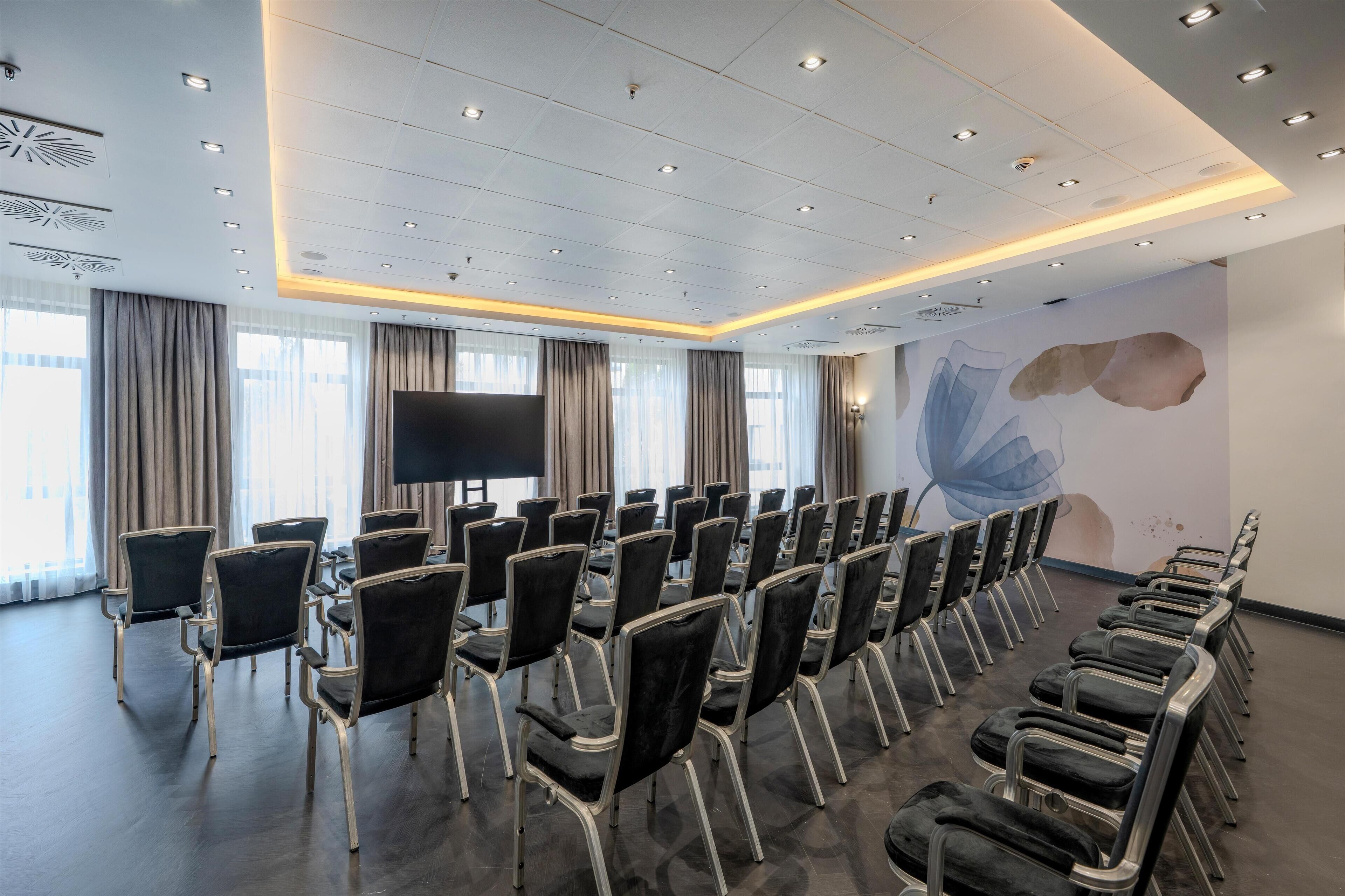 A conference room with rows of chairs, a large screen, and a modern ceiling design.