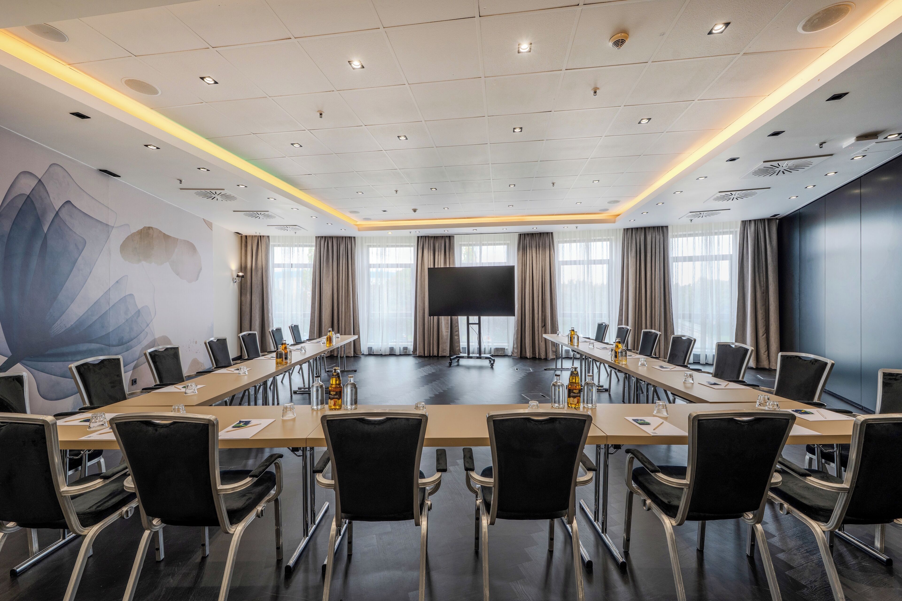 A conference room with a long table, black chairs, and a large screen at the front.