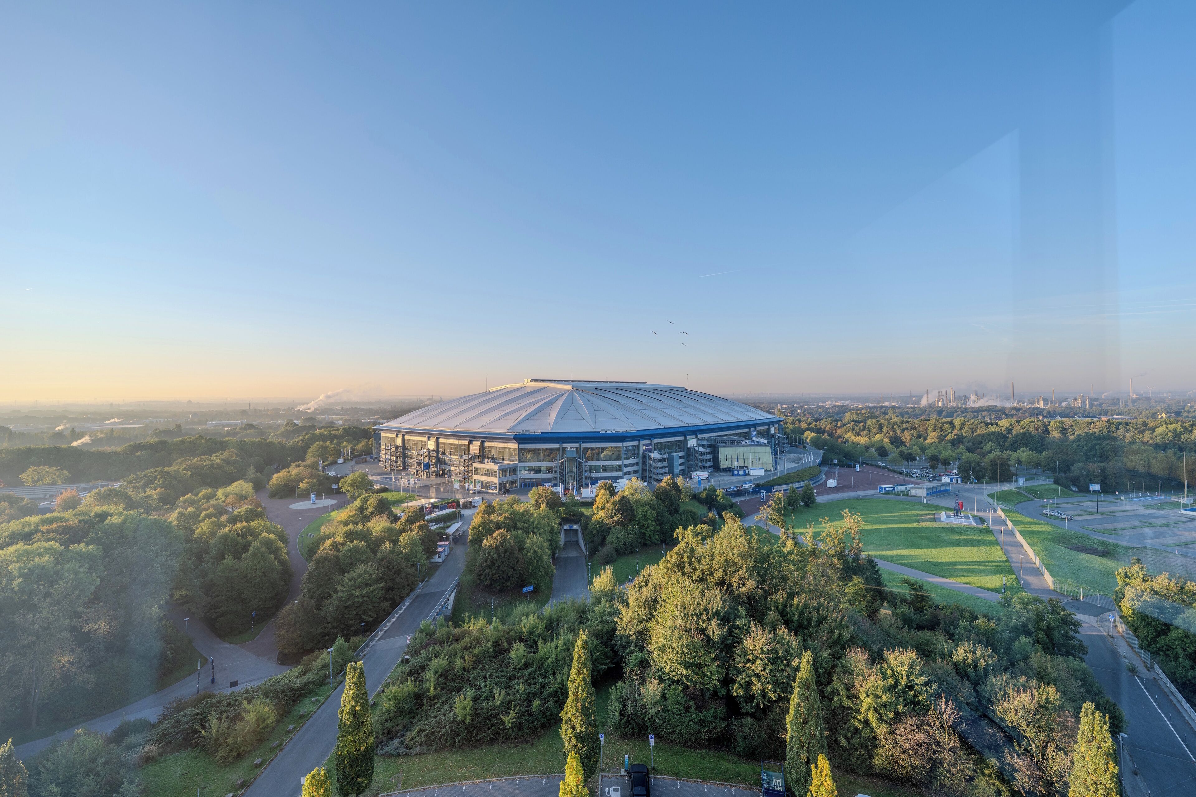 Ein Stadion, umgeben von Grünflächen und unter blauem Himmel.