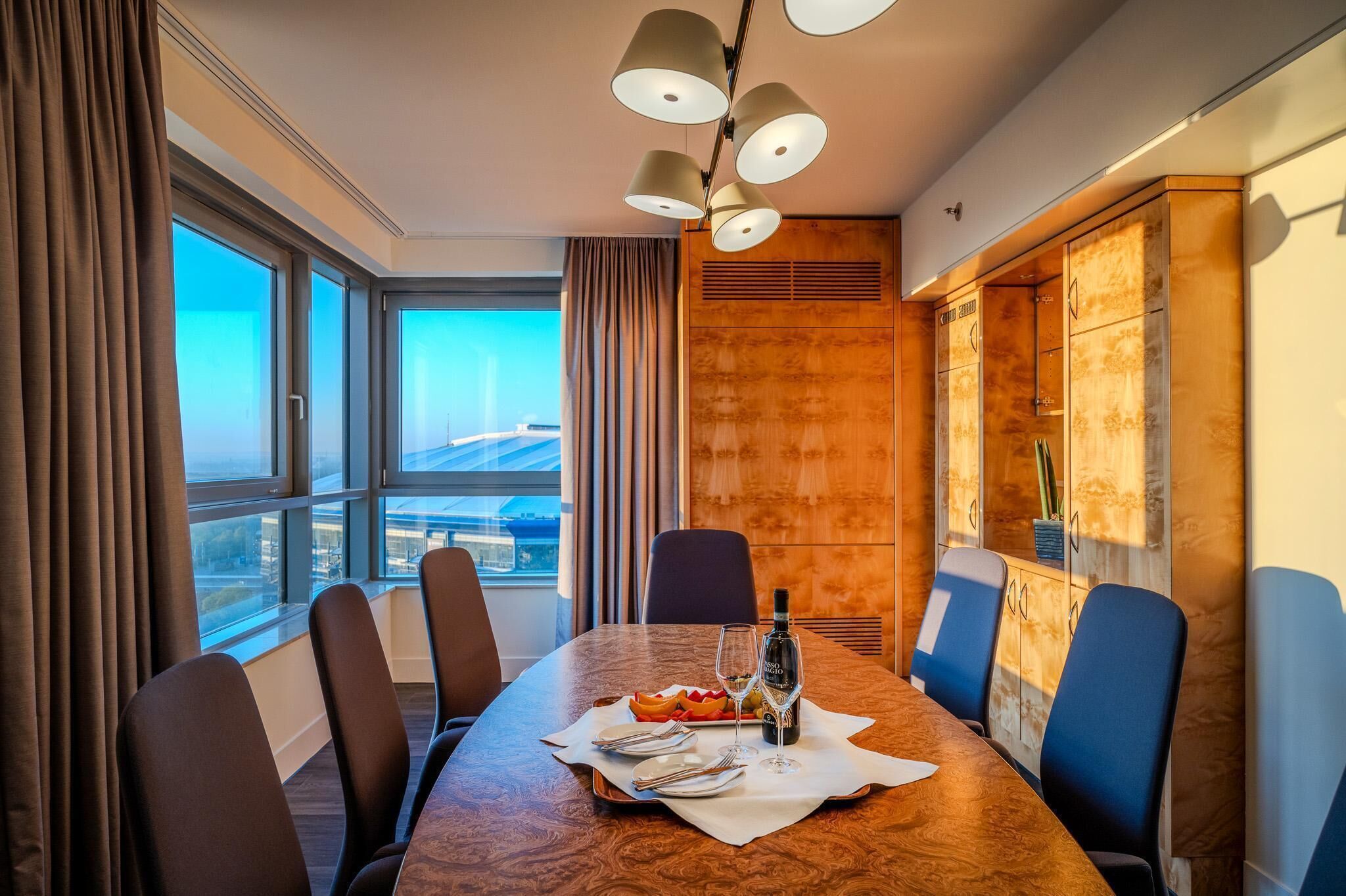 A conference room with a large table, chairs, a bottle of wine, and a fruit plate.
