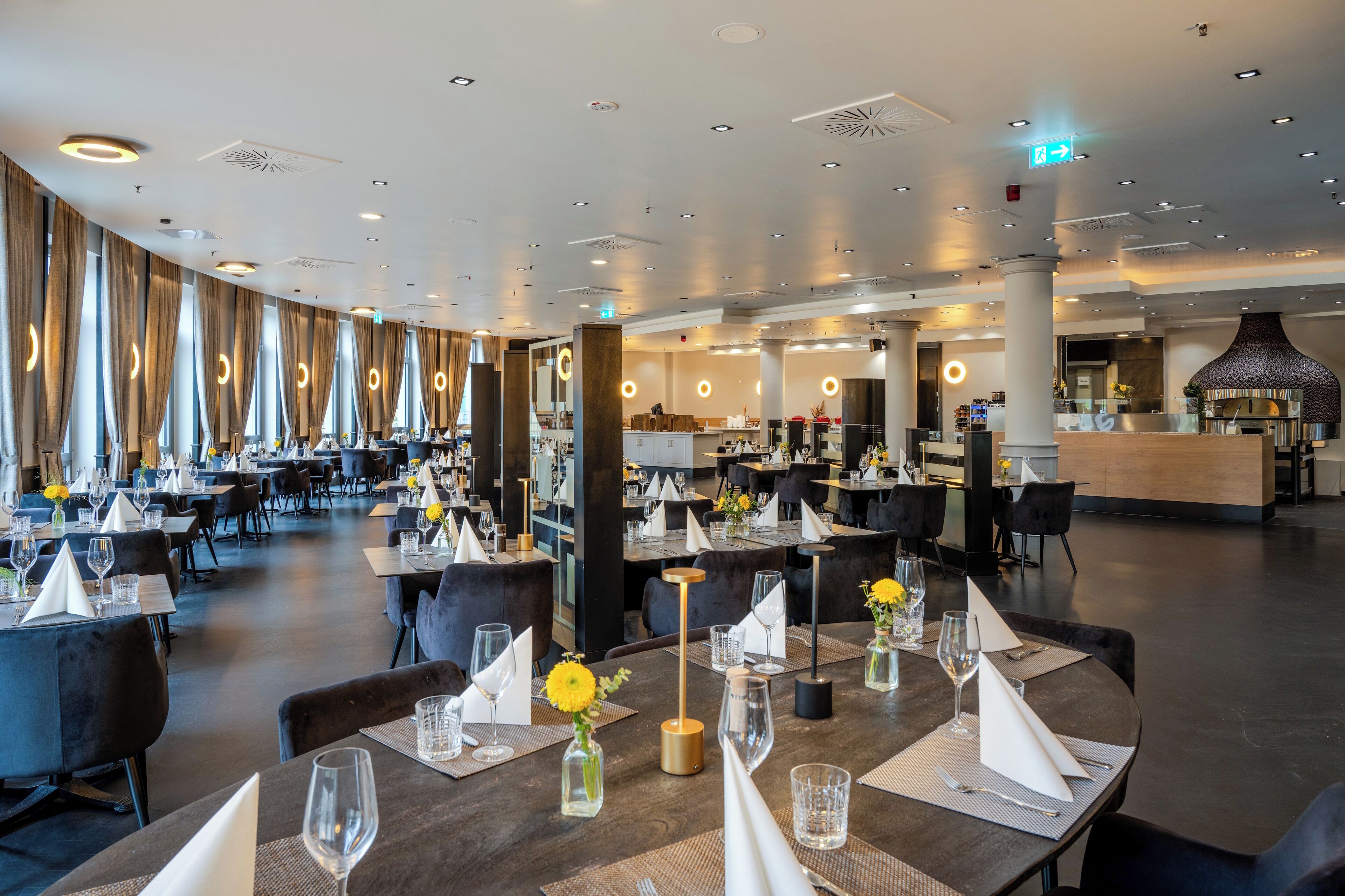 A spacious restaurant with multiple dining tables, each set with wine glasses and napkins, and a modern interior design.