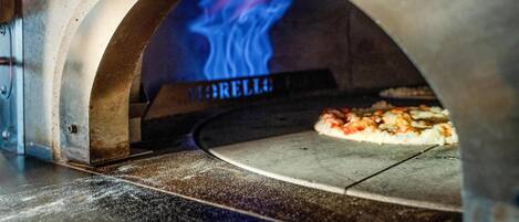 Un horno de pizza con fuego visible en su interior, una pizza horneándose y la palabra 'MARELLI' en la puerta del horno.