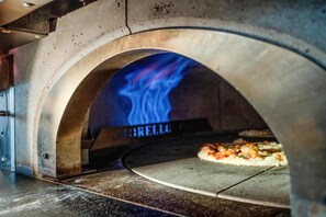 A pizza oven with a visible fire inside, a pizza being baked, and the word "MARELLI" on the oven door.