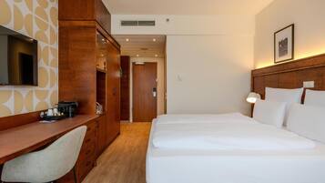 A hotel room with a wooden desk, a bed with white linens, and a television mounted on the wall.
