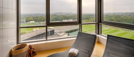 Una habitación con ventanas amplias, vista a un campo deportivo y dos sillones.