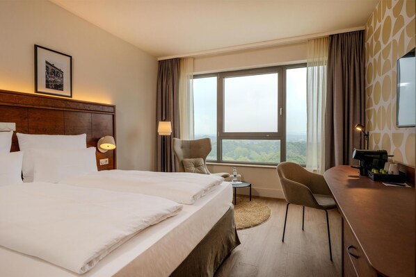 A hotel room with a large bed, a desk, a chair, a small table, and a window with a view.