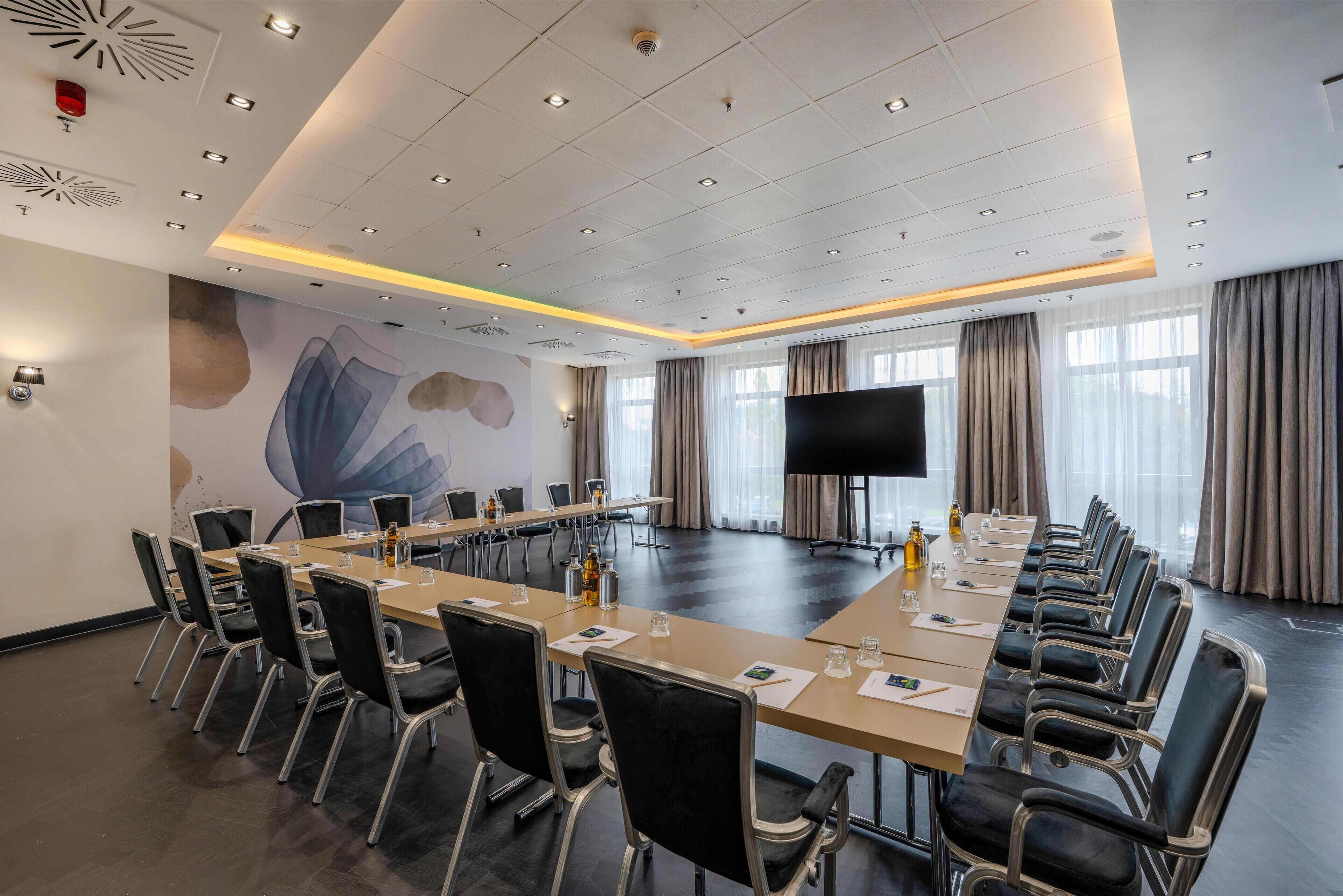 A conference room with a long table, chairs, a large screen, and a mural on the wall.