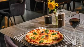 Eine Pizza auf einem Tisch, dazu ein Glas Rotwein und eine Vase mit Blumen.