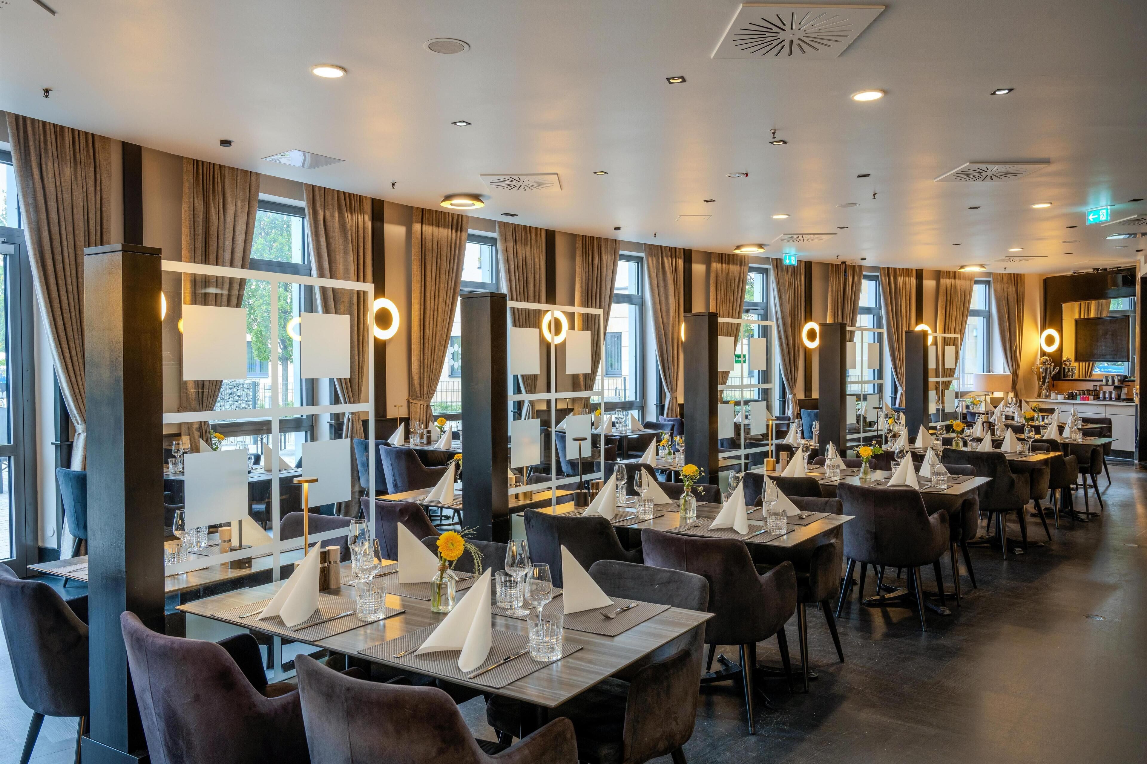 Ein modernes Restaurant mit mehreren Tischen, jeder Tisch gedeckt mit weißen Servietten, Gläsern und einer Blumenvase.