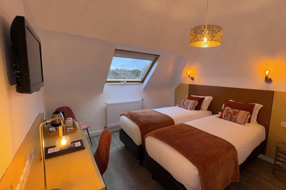 Une chambre d’hôtel avec deux lits, un bureau avec une chaise, une télévision, une fenêtre et un luminaire au plafond.