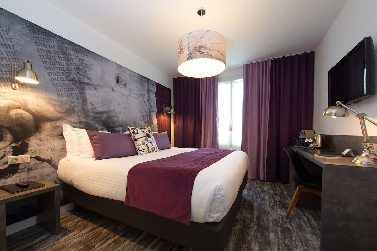 Une chambre d’hôtel moderne, dotée d’un grand lit, d’un bureau et d’une télévision.