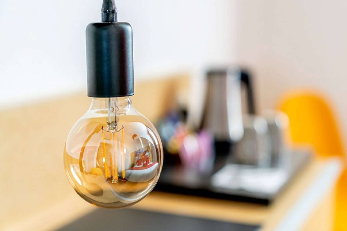 Une ampoule transparente, avec un culot noir, suspendue dans une pièce dont l’arrière-plan est flou.