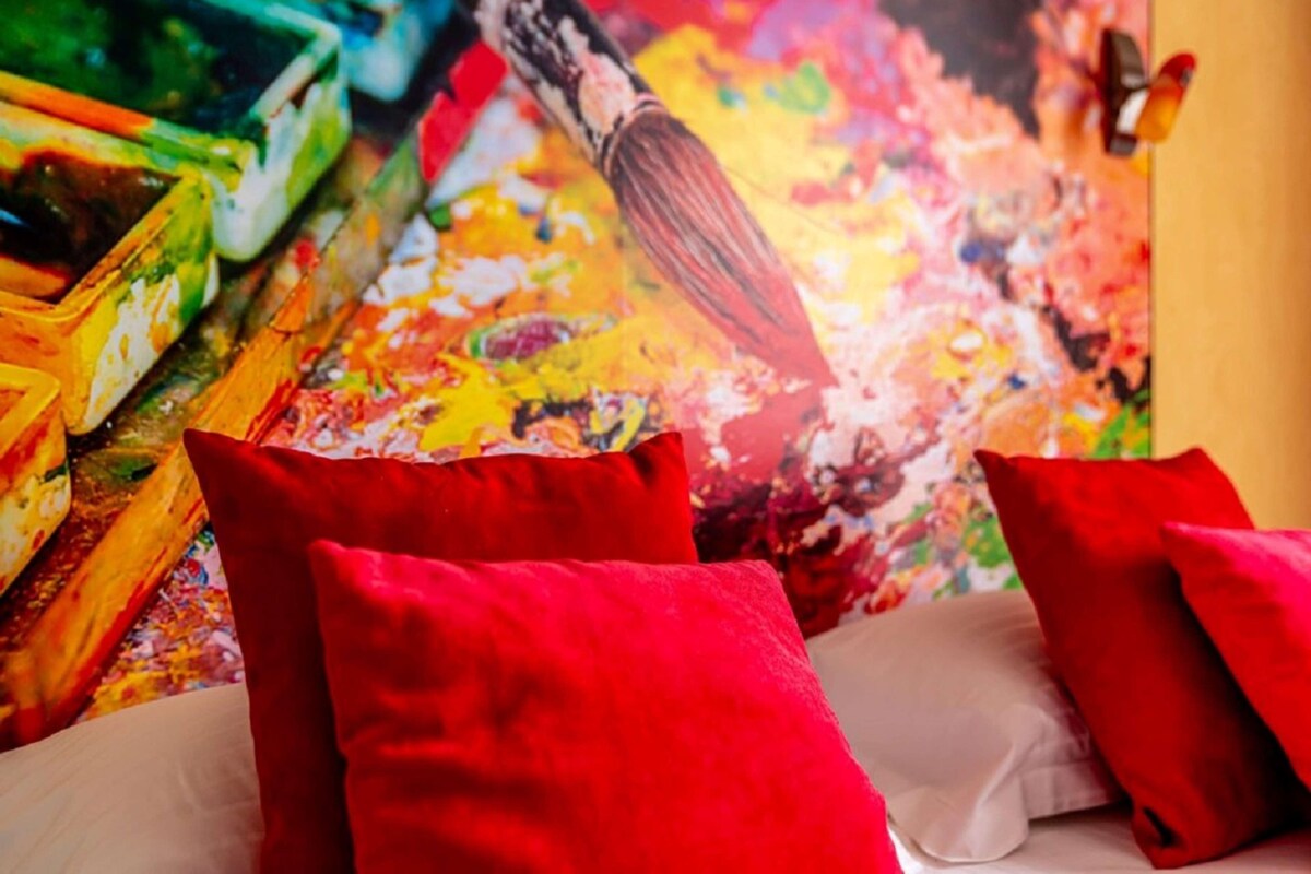 A bed with red pillows and a colorful abstract painting in the background.