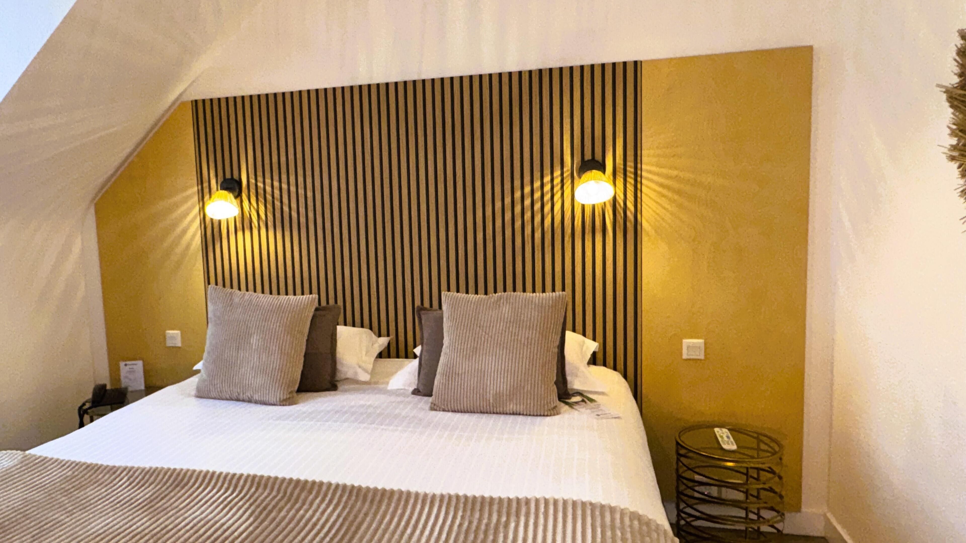 A bedroom with a sloped ceiling, a bed with pillows, and two wall-mounted lights.
