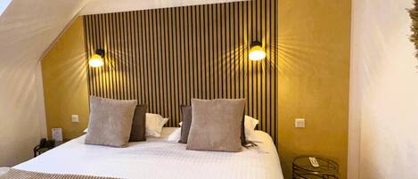 A bedroom with a sloped ceiling, a bed with pillows, and two wall-mounted lights.