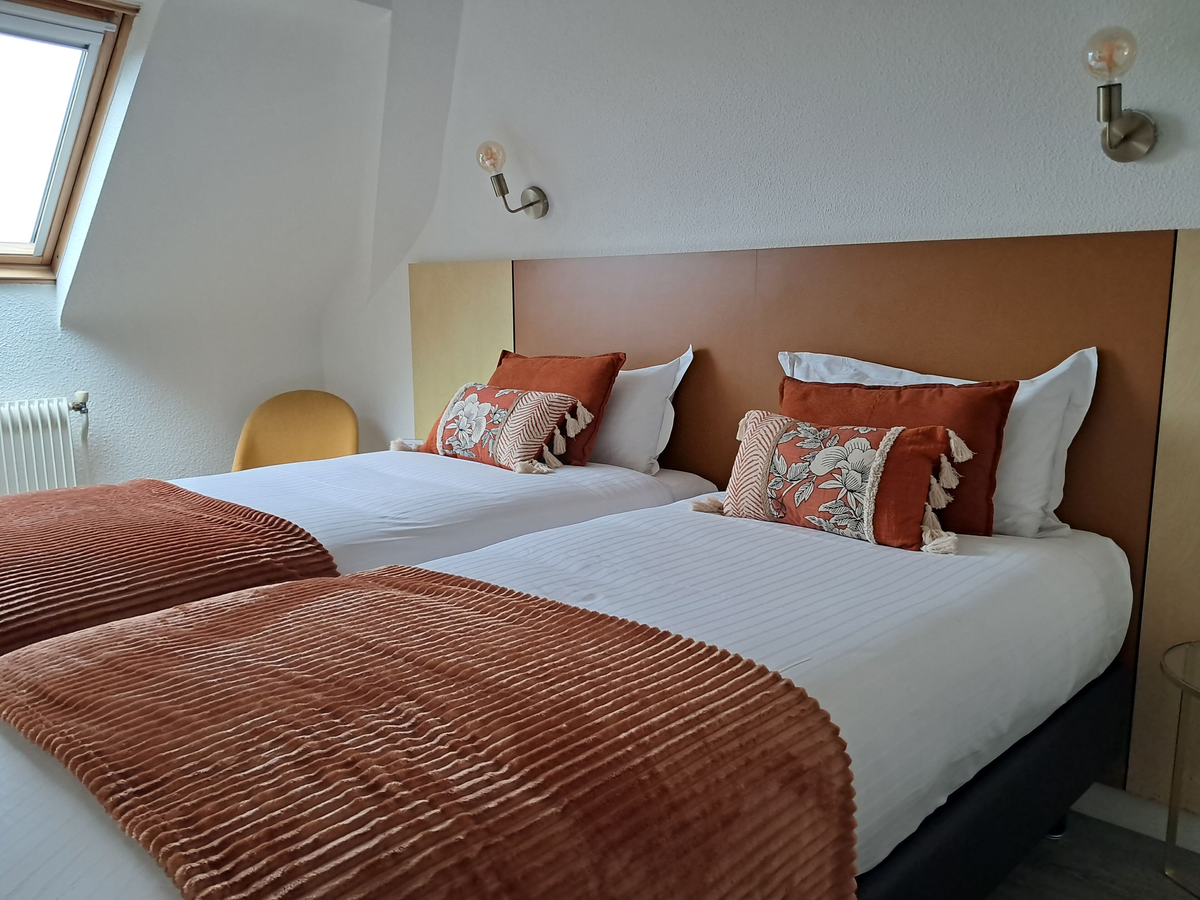 A hotel room with a large bed, two pillows, a headboard, and a bedside table.